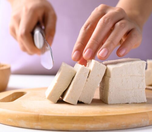 Photo shows someone cutting up a block of tofu. According to a scientist’s new scoring system, tofu is the single best protein for nutrition, sustainability, and affordability