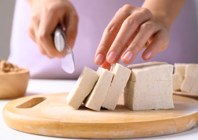Photo shows someone cutting up a block of tofu. According to a scientist’s new scoring system, tofu is the single best protein for nutrition, sustainability, and affordability