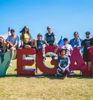 Photo shows the crew and organisers of Vegan Camp Out posing on a large "vegan" sign. Vegan Camp Out has announced the food lineup for this year’s festival