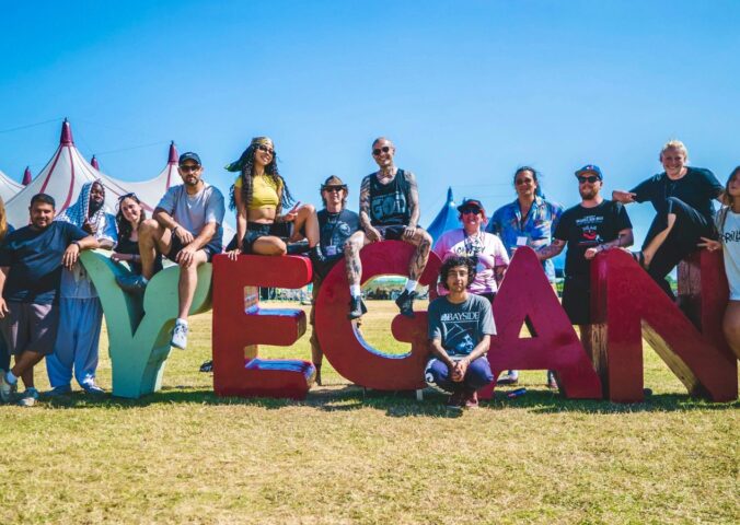 Photo shows the crew and organisers of Vegan Camp Out posing on a large "vegan" sign. Vegan Camp Out has announced the food lineup for this year’s festival