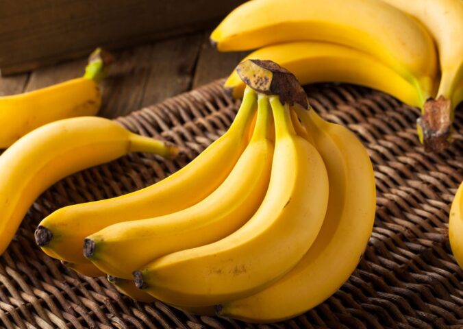 A bunch of ripe yellow bananas resting on a woven straw basket, to illustrate article about frozen and thawed bananas