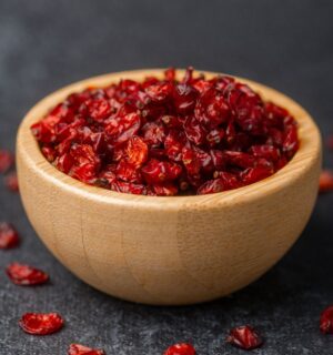 Dried barberries in a wooden bowl, with several berries spilled onto a black surface, to illustrate article about the berry that lowers cholesterol