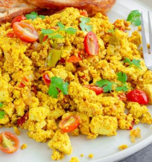 Tofu scramble with tomatoes and vegetables served on a white plate with toast and a fork to illustrate article comparing tofu vs eggs