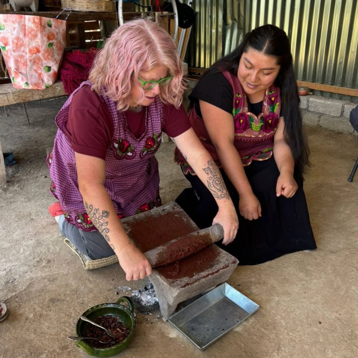 Photo shows a customer of Ahimsa Travel Club grinding flour by hand in Oxaca, Mexico, with instruction from someone local. Ahimsa Travel Club could help you take the vegan trip of your dreams