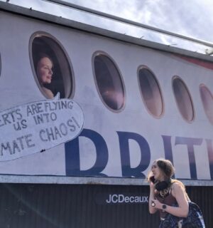 Photo shows a large billboard advertisement for British Airways that has been altered to read, "adverts are flying us into climate chaos," as a young woman walks in front. In a UK first, Bristol City Council has banned high-carbon ads