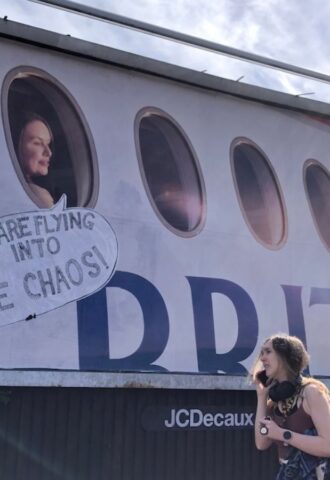 Photo shows a large billboard advertisement for British Airways that has been altered to read, "adverts are flying us into climate chaos," as a young woman walks in front. In a UK first, Bristol City Council has banned high-carbon ads