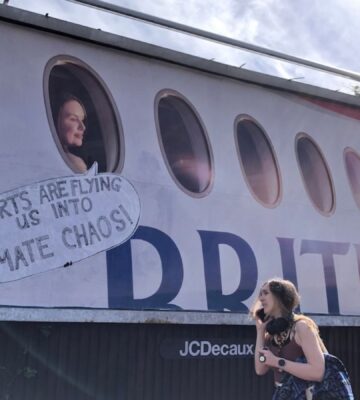 Photo shows a large billboard advertisement for British Airways that has been altered to read, "adverts are flying us into climate chaos," as a young woman walks in front. In a UK first, Bristol City Council has banned high-carbon ads