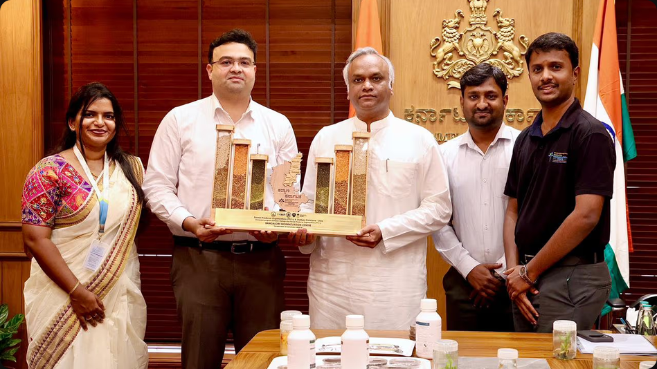 Photo shows staff from the Bangalore Bioinnovation Center (BBC) presenting a trophy made of wood and holding various legumes and pulses to Shri Priyank Kharge, the Minister for IT, Biotechnology, and e-Governance. BBC has partnered with the state agriculture department of Karnataka, India, to create a range of energy bars made with local pulses