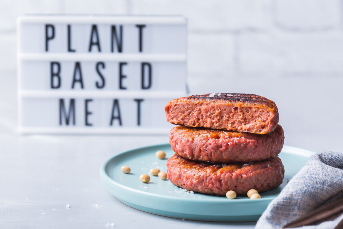 Photo shows a stack of plant-based burger patties in front of a sign that says, "plant-based meat." Lidl has announced a new range of blended animal meat products fortified with plant-based pea protein