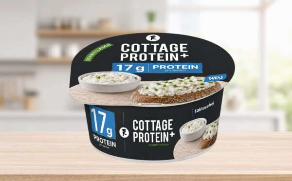 Photo shows the new vegan cottage cheese product, COTTAGE PROTEIN+, from Austrian food tech startup Revo Foods, against a stock kitchen background. The packaging is black, blue, and white. Revo Foods just launched a high-protein vegan cottage cheese made with fermented, upcycled apricot kernels