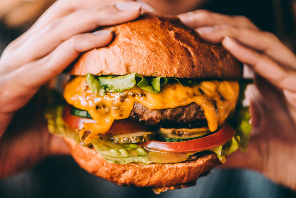 Photo shows someone's hands holding a large cheeseburger. A team of scientists has grown microalgae from cultivated meat production waste