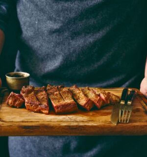 Photo shows a man holding a wooden chopping board with a rare steak, knife, and fork on it. Episode two of Stacey Dooley’s new TV show, Clickbait Clinic, tackles the carnivore diet