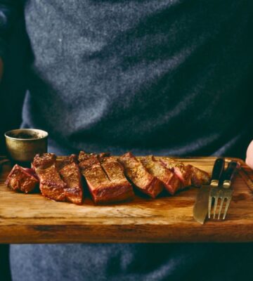 Photo shows a man holding a wooden chopping board with a rare steak, knife, and fork on it. Episode two of Stacey Dooley’s new TV show, Clickbait Clinic, tackles the carnivore diet