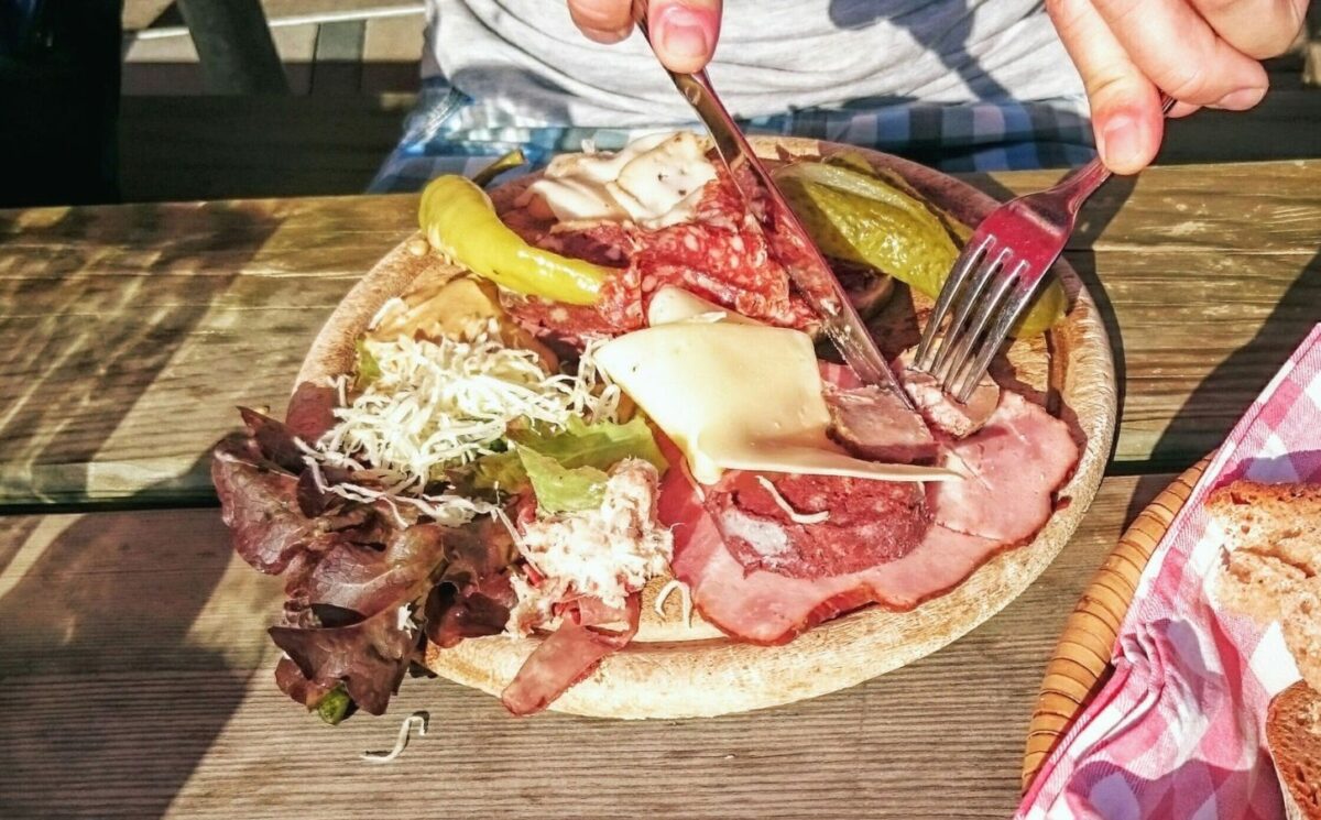 Photo shows someone eating a large plate of various different meats and cheeses on a picnic table in Switzerland. A new study has found that Switzerland’s meat and dairy consumption is up to 850 percent higher than recommended by the EAT-Lancet Planetary Health Diet. The study also found that many Swiss people significantly “underconsume” key plant-based foods, such as legumes