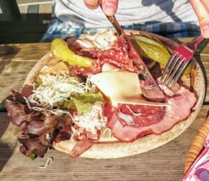 Photo shows someone eating a large plate of various different meats and cheeses on a picnic table in Switzerland. A new study has found that Switzerland’s meat and dairy consumption is up to 850 percent higher than recommended by the EAT-Lancet Planetary Health Diet. The study also found that many Swiss people significantly “underconsume” key plant-based foods, such as legumes