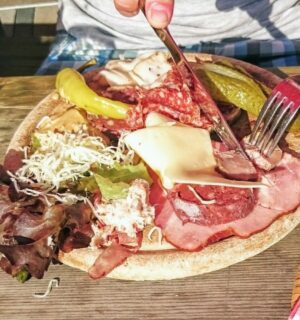 Photo shows someone eating a large plate of various different meats and cheeses on a picnic table in Switzerland. A new study has found that Switzerland’s meat and dairy consumption is up to 850 percent higher than recommended by the EAT-Lancet Planetary Health Diet. The study also found that many Swiss people significantly “underconsume” key plant-based foods, such as legumes