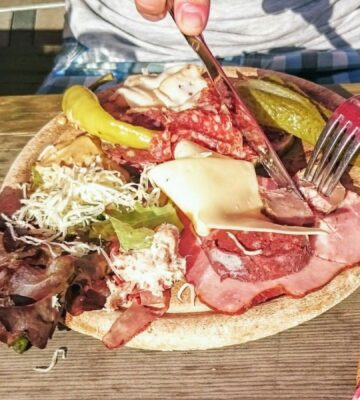 Photo shows someone eating a large plate of various different meats and cheeses on a picnic table in Switzerland. A new study has found that Switzerland’s meat and dairy consumption is up to 850 percent higher than recommended by the EAT-Lancet Planetary Health Diet. The study also found that many Swiss people significantly “underconsume” key plant-based foods, such as legumes