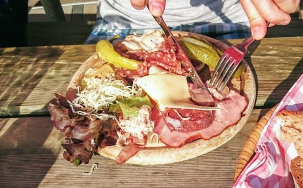 Photo shows someone eating a large plate of various different meats and cheeses on a picnic table in Switzerland. A new study has found that Switzerland’s meat and dairy consumption is up to 850 percent higher than recommended by the EAT-Lancet Planetary Health Diet. The study also found that many Swiss people significantly “underconsume” key plant-based foods, such as legumes
