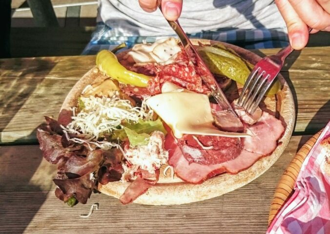Photo shows someone eating a large plate of various different meats and cheeses on a picnic table in Switzerland. A new study has found that Switzerland’s meat and dairy consumption is up to 850 percent higher than recommended by the EAT-Lancet Planetary Health Diet. The study also found that many Swiss people significantly “underconsume” key plant-based foods, such as legumes