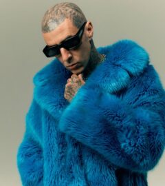 Photo shows Travis Barker wearing sunglasses and a blue faux fur coat. In a new promotional video for Humane World for Animals, Travis Barker encourages people to “do some good” for animals