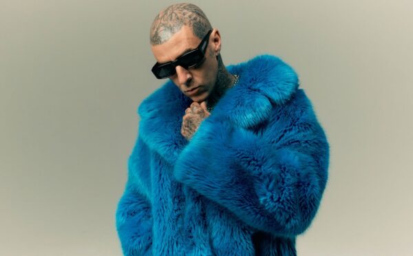 Photo shows Travis Barker wearing sunglasses and a blue faux fur coat. In a new promotional video for Humane World for Animals, Travis Barker encourages people to “do some good” for animals