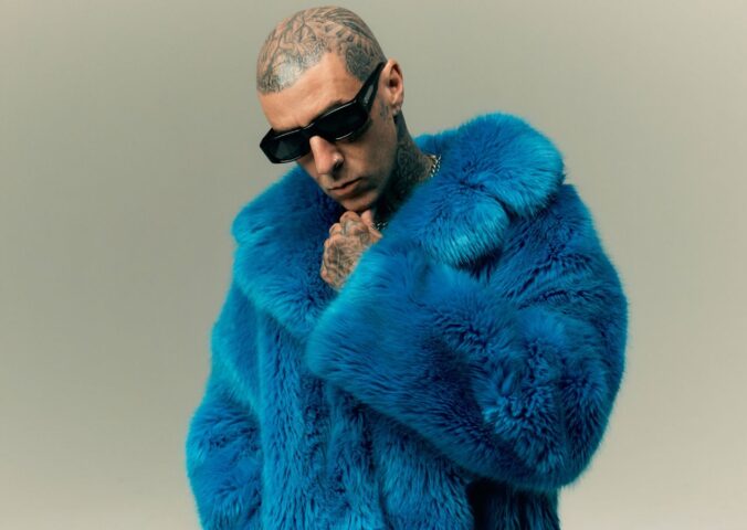 Photo shows Travis Barker wearing sunglasses and a blue faux fur coat. In a new promotional video for Humane World for Animals, Travis Barker encourages people to “do some good” for animals