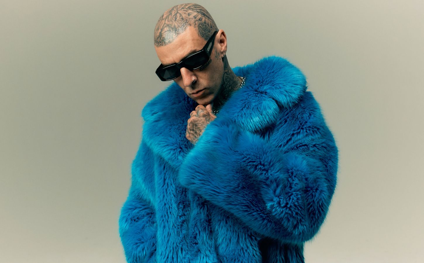 Photo shows Travis Barker wearing sunglasses and a blue faux fur coat. In a new promotional video for Humane World for Animals, Travis Barker encourages people to “do some good” for animals
