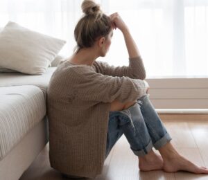 Photo shows a woman sitting on the floor and looking out a window with her forehead resting on her hand. Depression may involve more than brain chemistry, with inflammation, diet, the microbiome and the gut-brain connection also playing a role