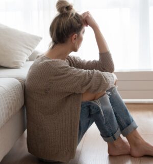 Photo shows a woman sitting on the floor and looking out a window with her forehead resting on her hand. Depression may involve more than brain chemistry, with inflammation, diet, the microbiome and the gut-brain connection also playing a role