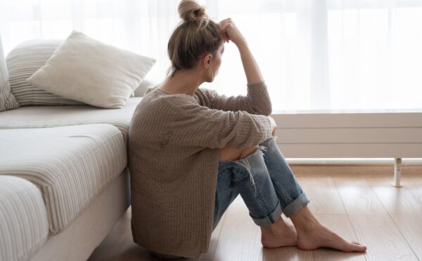 Photo shows a woman sitting on the floor and looking out a window with her forehead resting on her hand. Depression may involve more than brain chemistry, with inflammation, diet, the microbiome and the gut-brain connection also playing a role