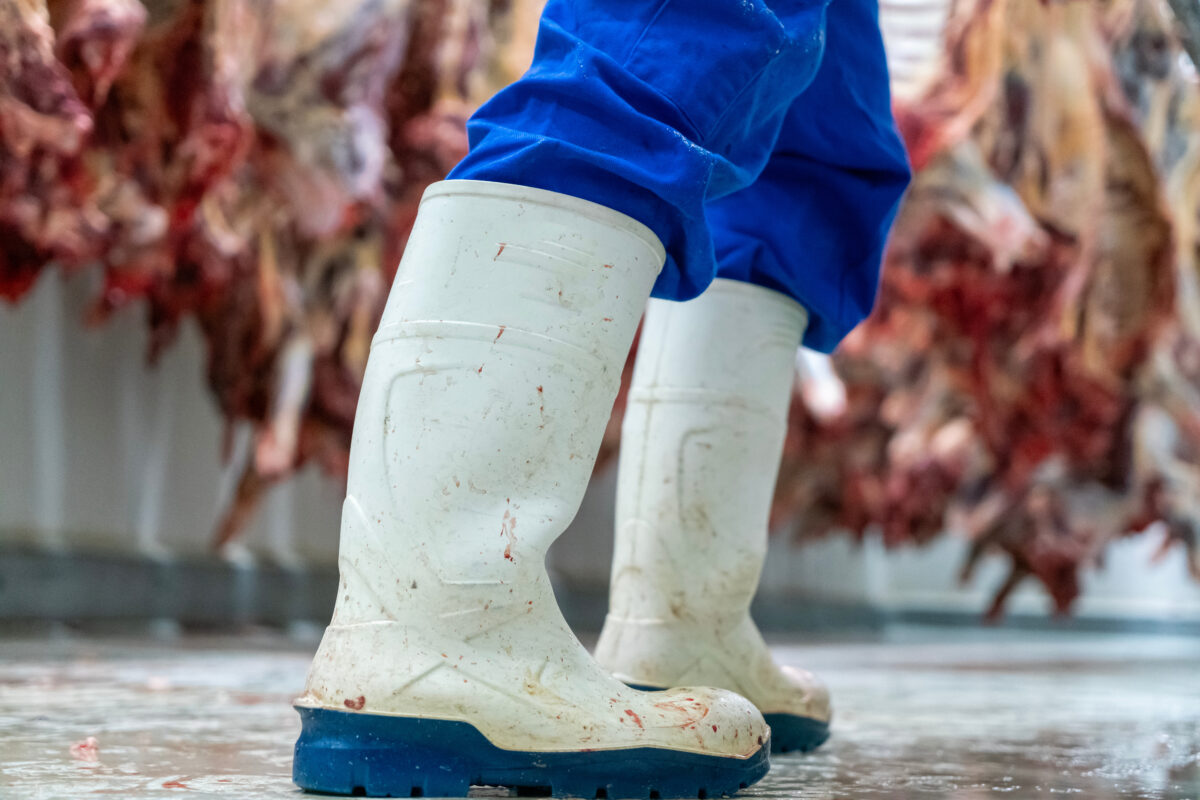 Photo shows a meat packing plant worker's white rubber boots, spattered with blood, and skinless dead animals hung up in the background. Roughly 100 workers have walked out of a Smithfield meat plant following a colleague’s death