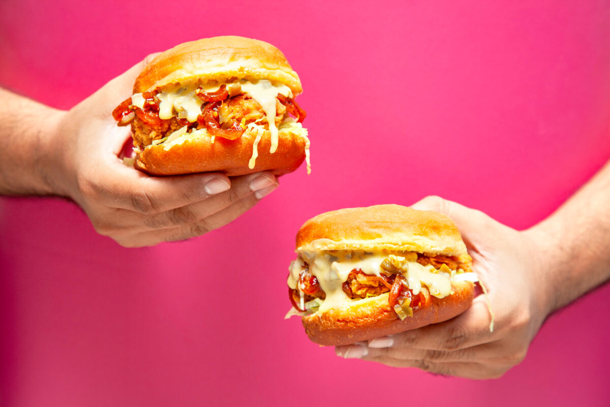 Photo shows hands holding two large burgers. New research has found that most consumers in urban India would buy cultivated meat