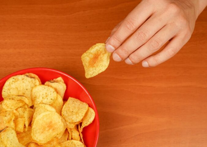 Photo shows someone's hand as they reach for a large red bowl of crisps. Crisps with “meaty” names and flavors like roast chicken could soon be caught up in the EU’s controversial plant-based labeling ban
