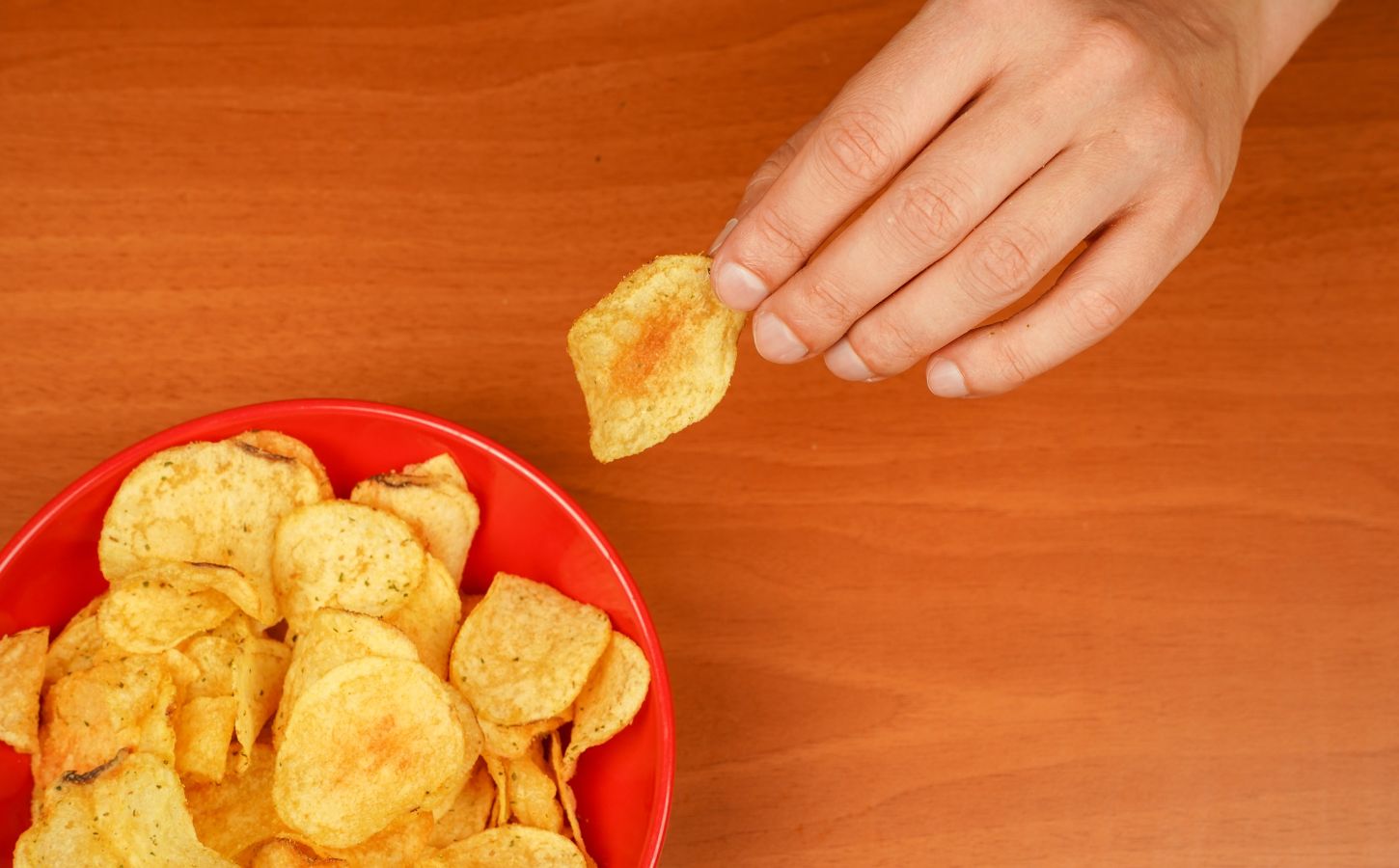 Photo shows someone's hand as they reach for a large red bowl of crisps. Crisps with “meaty” names and flavors like roast chicken could soon be caught up in the EU’s controversial plant-based labeling ban