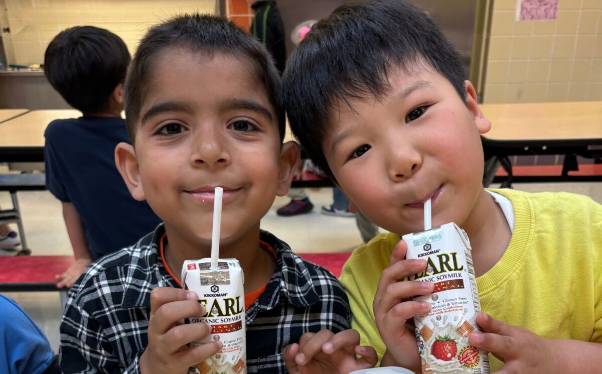 Photo shows two kids drinking soy milk out of cartons during school lunch. New data shows that a soy milk pilot program in New York City (NYC) schools found strong student demand and reduced greenhouse gas emissions (GHGs) by 17.4 percent