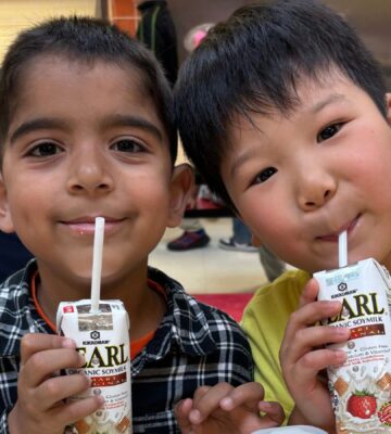 Photo shows two kids drinking soy milk out of cartons during school lunch. New data shows that a soy milk pilot program in New York City (NYC) schools found strong student demand and reduced greenhouse gas emissions (GHGs) by 17.4 percent