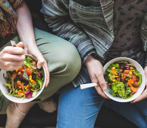 Photo shows two people holding bowls of colorful vegetables and other plant foods. Most people in the UK would be willing to cut their meat and dairy consumption in order to improve food security, according to a new survey