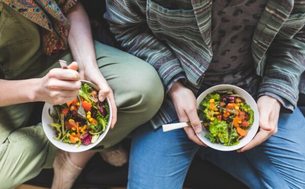 Photo shows two people holding bowls of colorful vegetables and other plant foods. Most people in the UK would be willing to cut their meat and dairy consumption in order to improve food security, according to a new survey