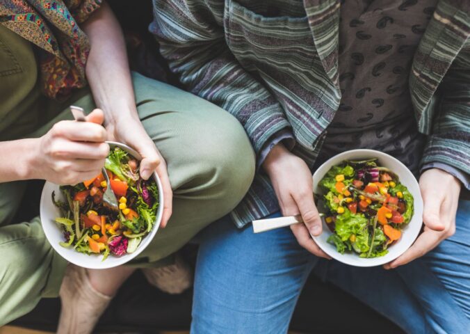 Photo shows two people holding bowls of colorful vegetables and other plant foods. Most people in the UK would be willing to cut their meat and dairy consumption in order to improve food security, according to a new survey